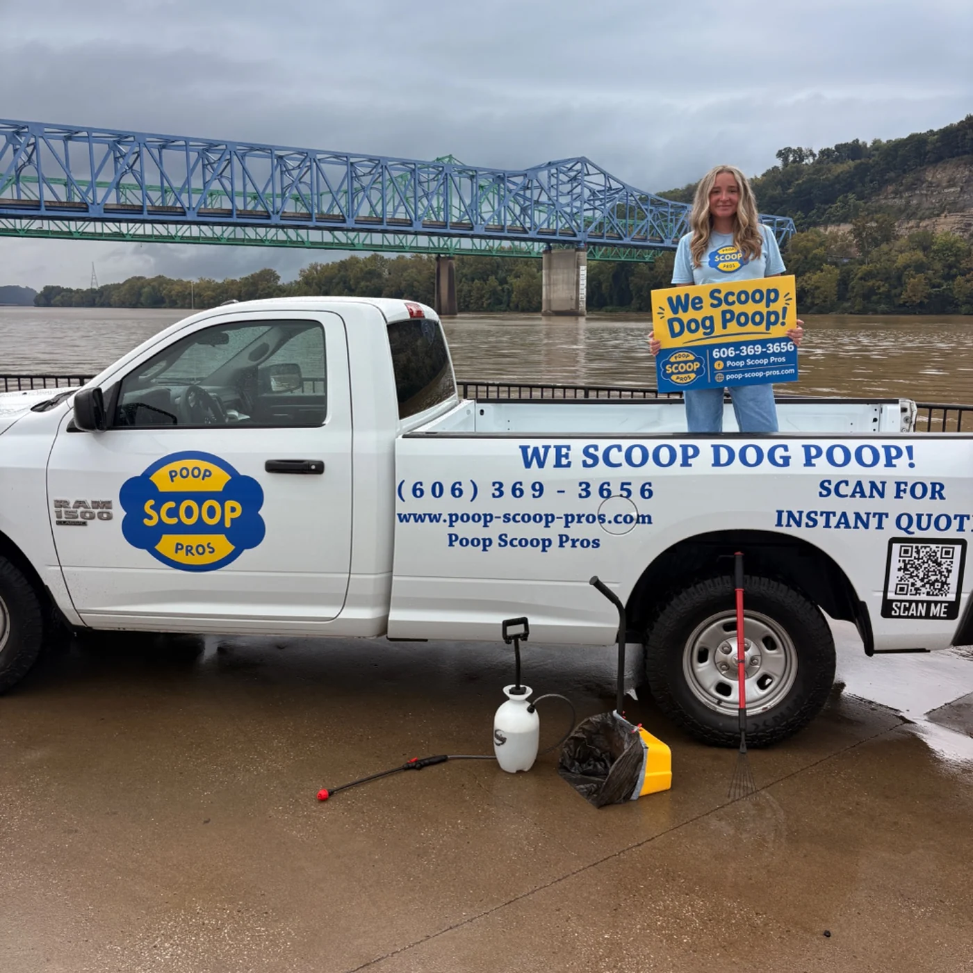 Poop Scoop Pros team member holding the company sign in the branded truck, with the blue bridge behind